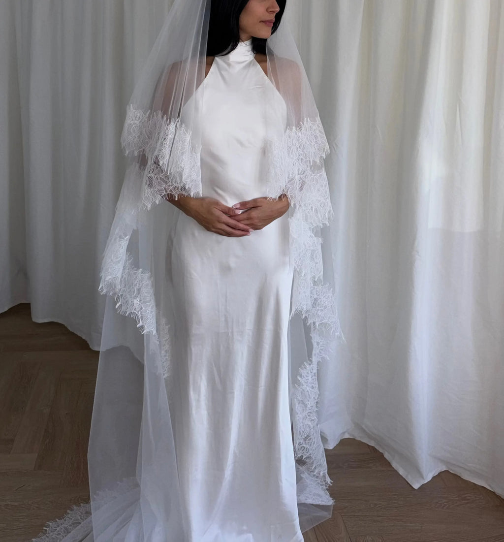 This cathedral-length lace trim blusher wedding veil flows gracefully behind the bride, made from soft, lightweight tulle and finished with intricate lace trim. Ideal for traditional or formal weddings, it creates a striking, romantic silhouette and complements any bridal gown with elegance and sophistication.