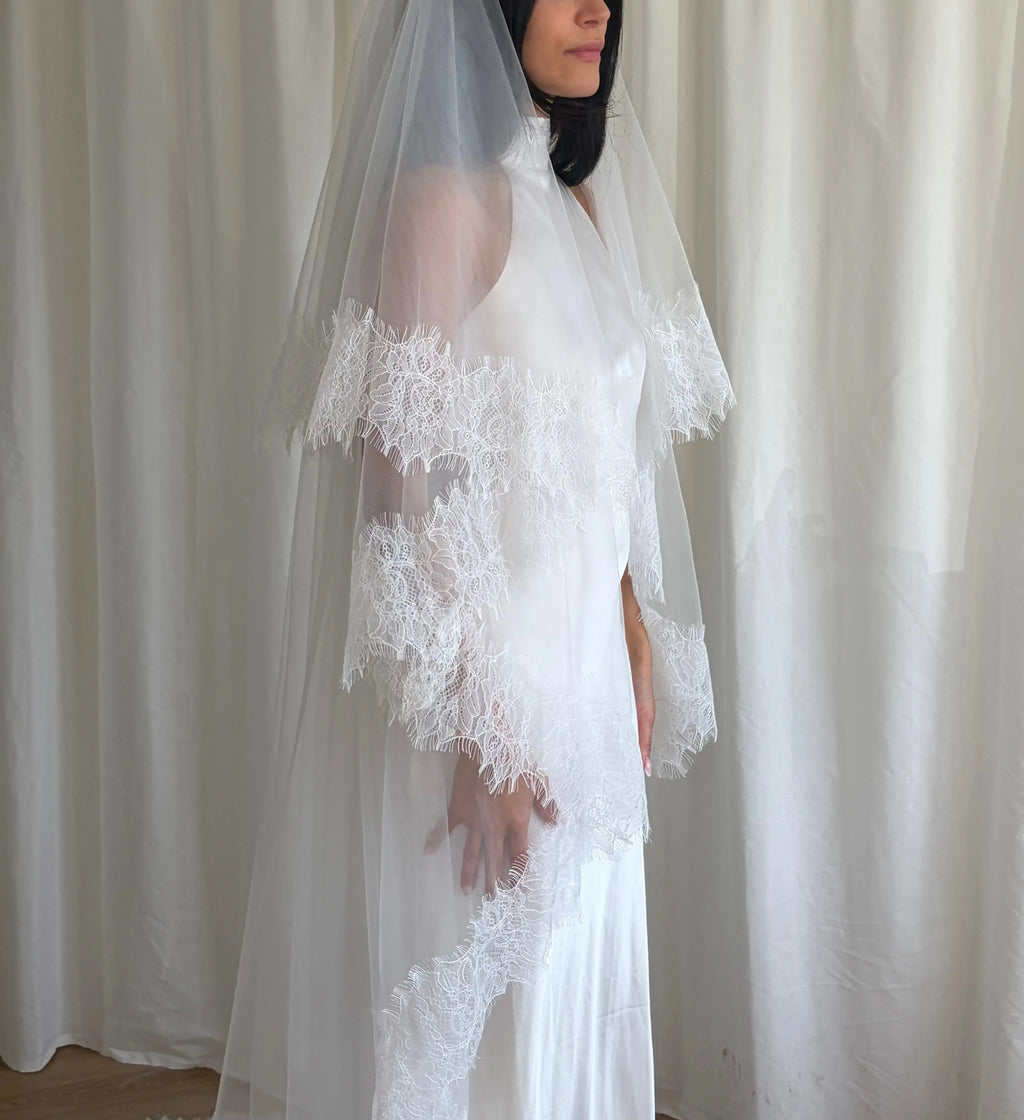 This cathedral-length lace trim blusher wedding veil flows gracefully behind the bride, made from soft, lightweight tulle and finished with intricate lace trim. Ideal for traditional or formal weddings, it creates a striking, romantic silhouette and complements any bridal gown with elegance and sophistication.
