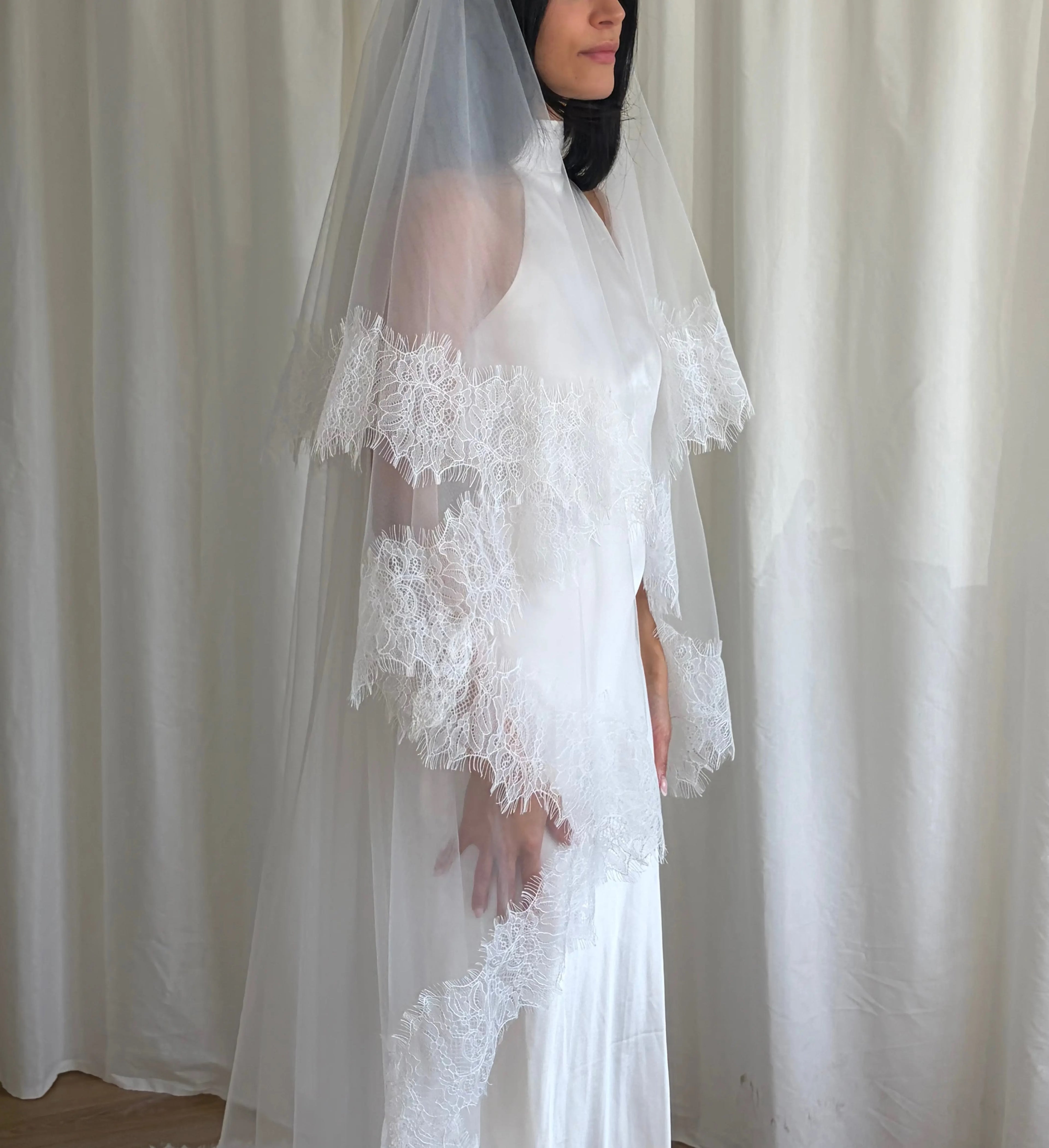 This cathedral-length lace trim blusher wedding veil flows gracefully behind the bride, made from soft, lightweight tulle and finished with intricate lace trim. Ideal for traditional or formal weddings, it creates a striking, romantic silhouette and complements any bridal gown with elegance and sophistication.