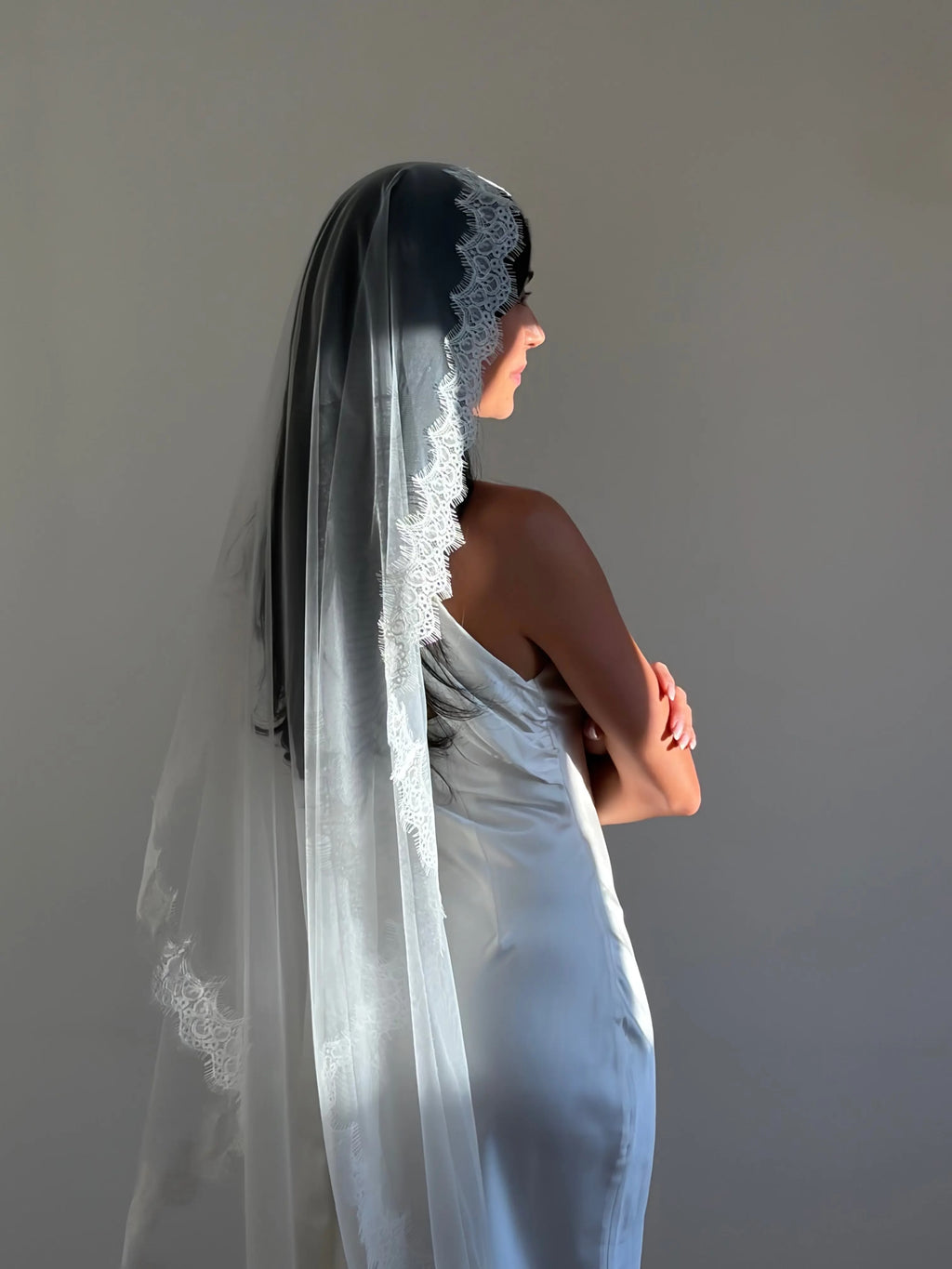 The Mantilla French Chantilly Lace Cathedral-Length Veil captures the romance of classic bridal style with exquisite craftsmanship and detail. Made from fine, lightweight tulle, this single-tier veil is bordered with intricate French Chantilly floral lace, complete with delicate eyelash edging that adds soft texture and movement. Its cathedral length creates a graceful, dramatic silhouette perfect for traditional or contemporary gowns. A hidden comb ensures a secure, comfortable hold, letting the veil flow 