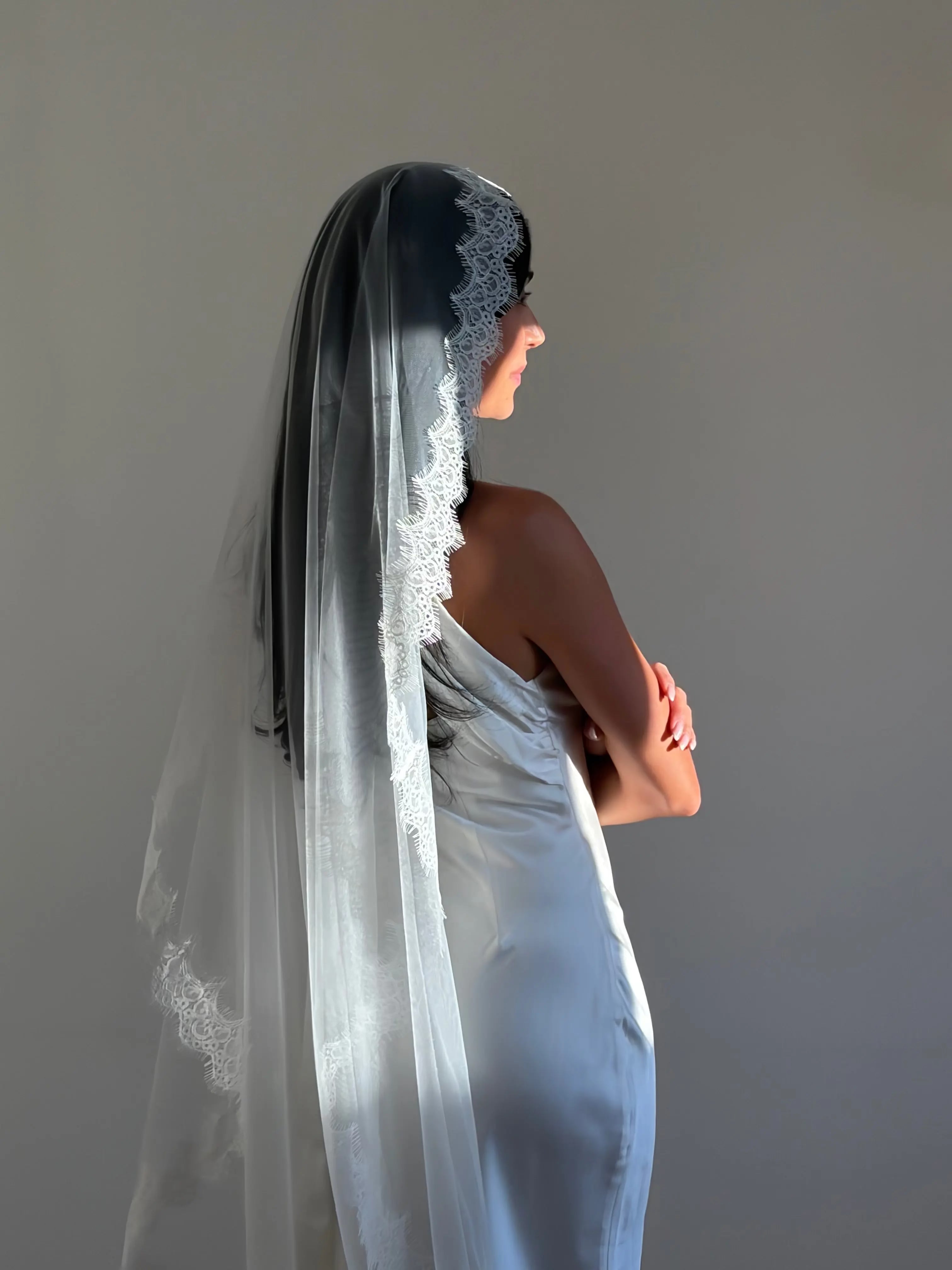 The Mantilla French Chantilly Lace Cathedral-Length Veil captures the romance of classic bridal style with exquisite craftsmanship and detail. Made from fine, lightweight tulle, this single-tier veil is bordered with intricate French Chantilly floral lace, complete with delicate eyelash edging that adds soft texture and movement. Its cathedral length creates a graceful, dramatic silhouette perfect for traditional or contemporary gowns. A hidden comb ensures a secure, comfortable hold, letting the veil flow 