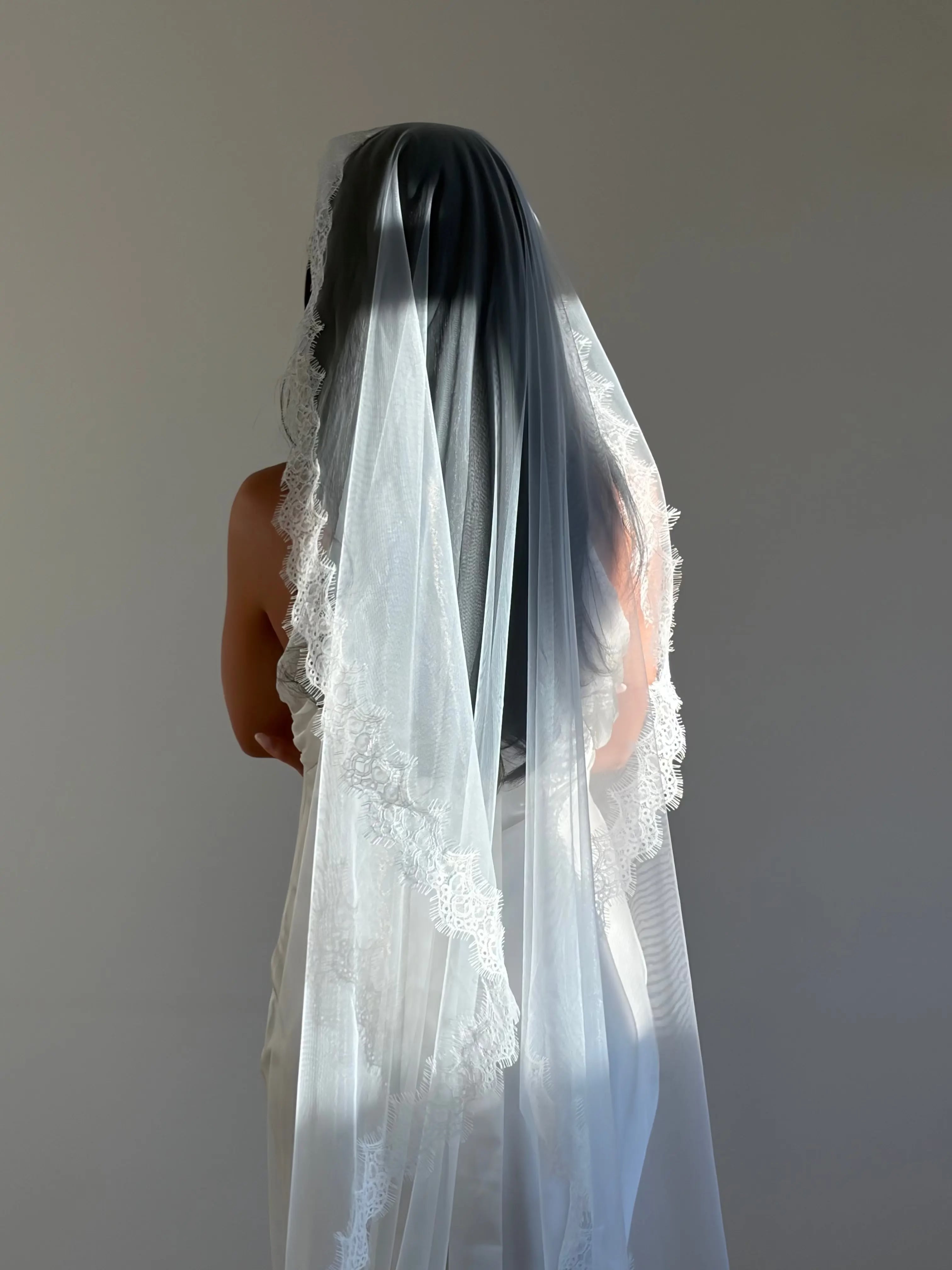 The Mantilla French Chantilly Lace Cathedral-Length Veil captures the romance of classic bridal style with exquisite craftsmanship and detail. Made from fine, lightweight tulle, this single-tier veil is bordered with intricate French Chantilly floral lace, complete with delicate eyelash edging that adds soft texture and movement. Its cathedral length creates a graceful, dramatic silhouette perfect for traditional or contemporary gowns. A hidden comb ensures a secure, comfortable hold, letting the veil flow 