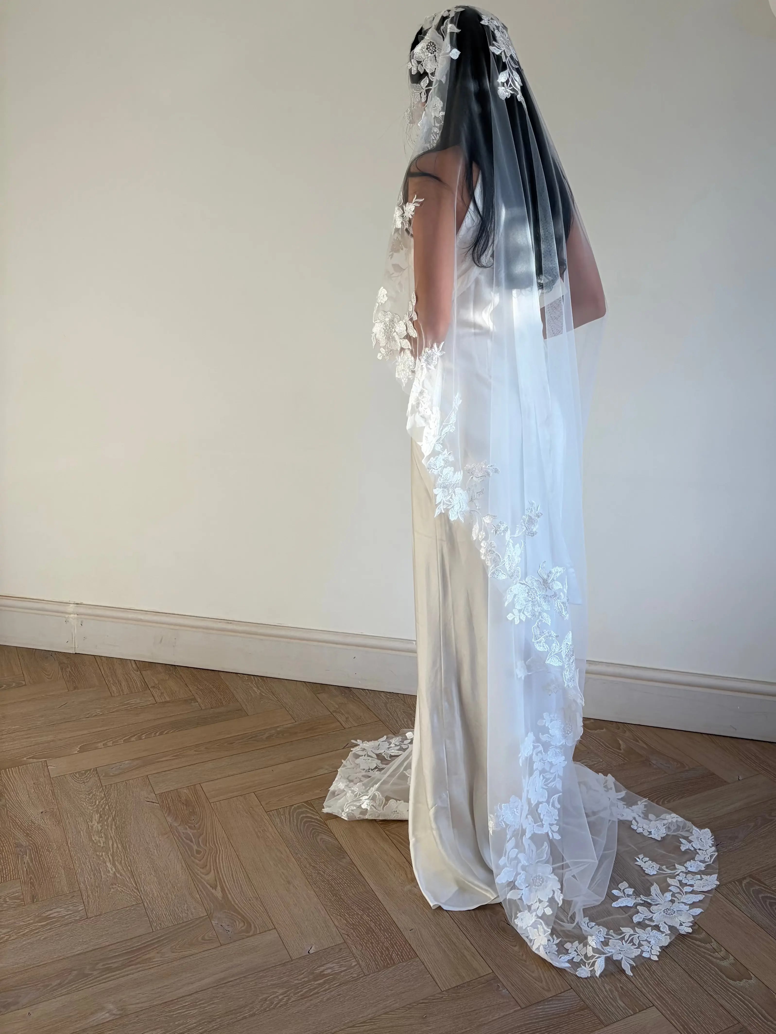 The Embroidered Ethereal Garden Floral Lace Veil features fine sequin embroidery and hand-finished floral lace trim for a soft, ethereal glow. Crafted from luxurious tulle in a soft off-white tone, this romantic bridal veil drapes beautifully for a fairytale-inspired finish. Perfect for garden or cathedral weddings.