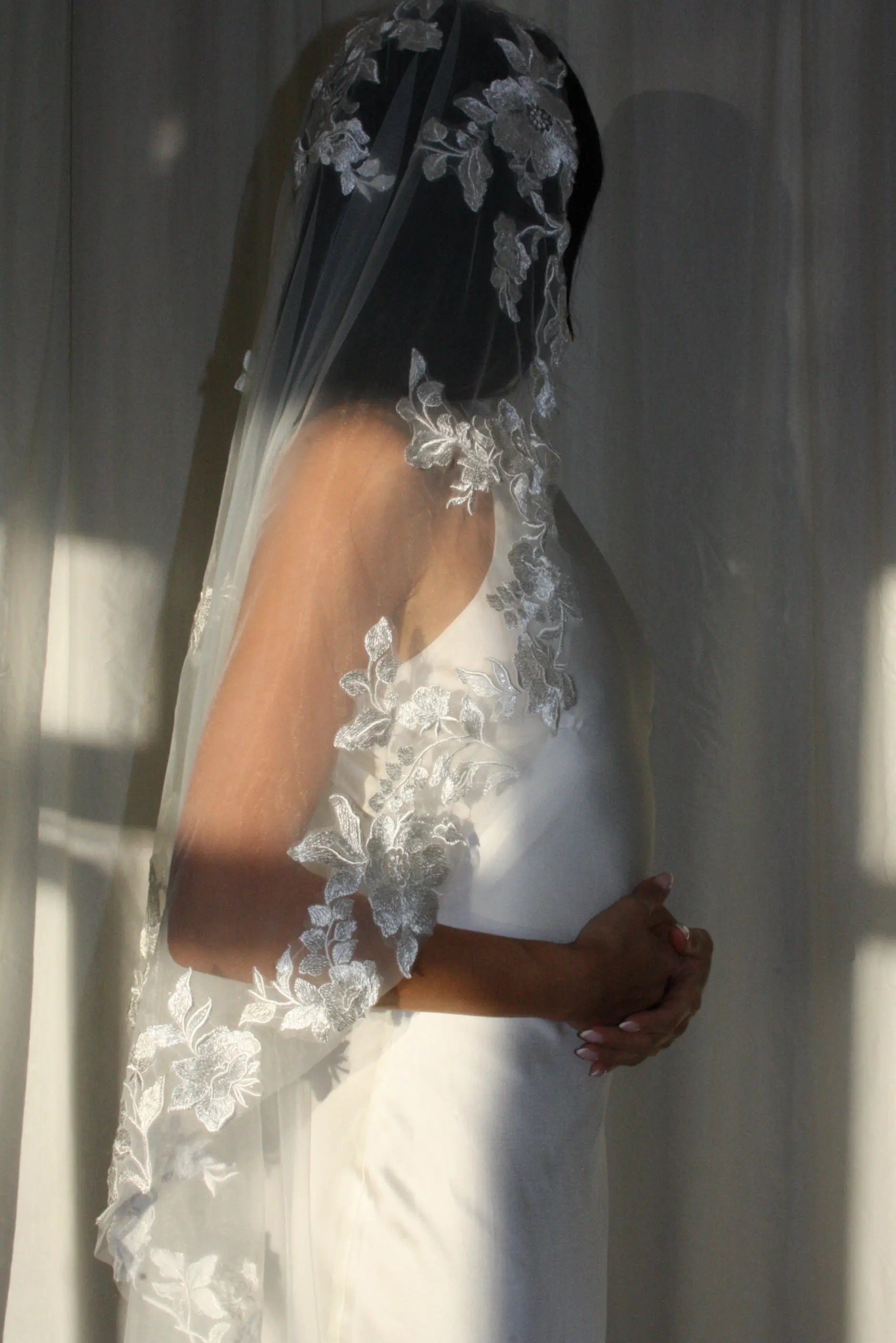 The Embroidered Ethereal Garden Floral Lace Veil features fine sequin embroidery and hand-finished floral lace trim for a soft, ethereal glow. Crafted from luxurious tulle in a soft off-white tone, this romantic bridal veil drapes beautifully for a fairytale-inspired finish. Perfect for garden or cathedral weddings.