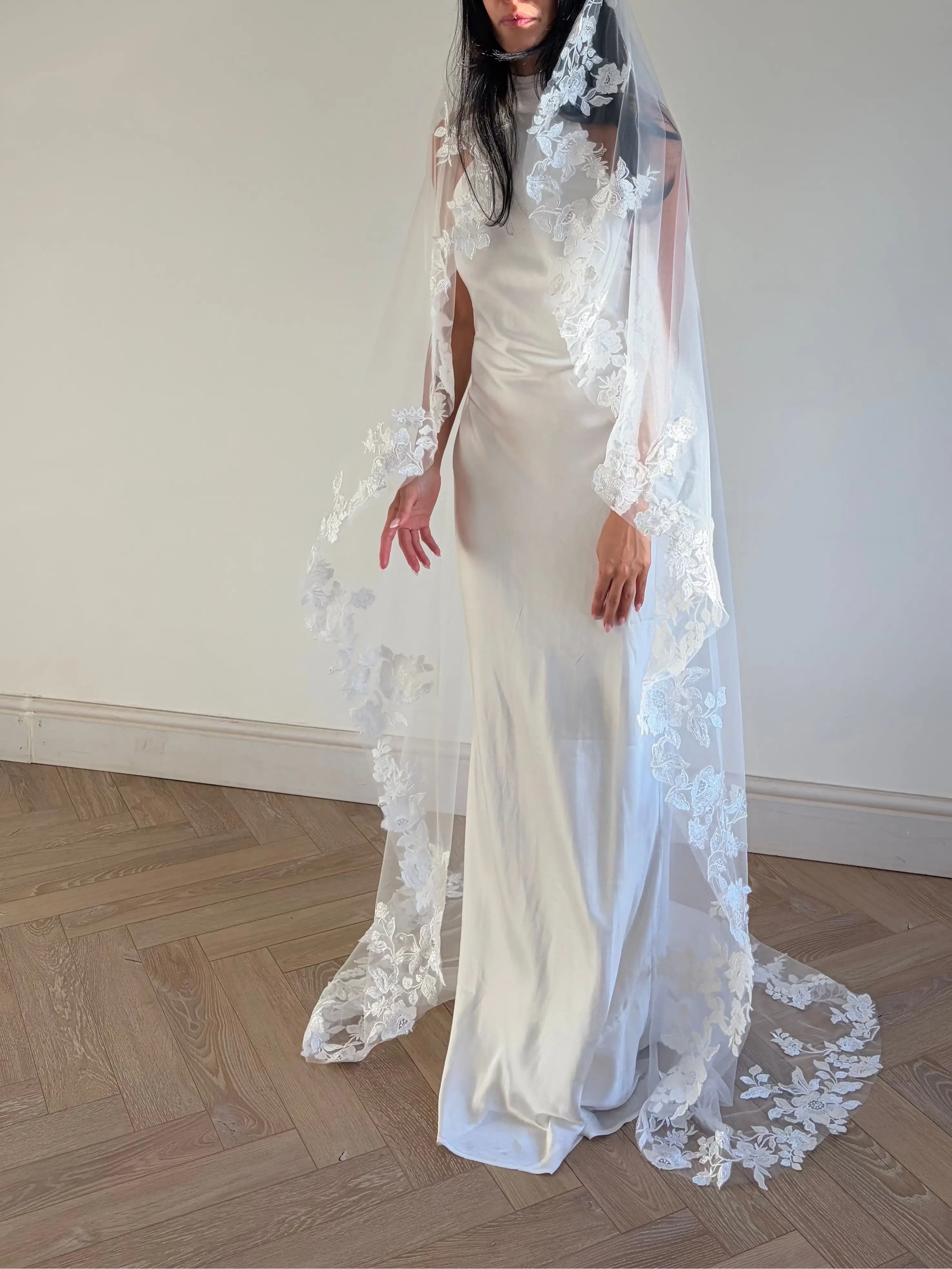 The Embroidered Ethereal Garden Floral Lace Veil features fine sequin embroidery and hand-finished floral lace trim for a soft, ethereal glow. Crafted from luxurious tulle in a soft off-white tone, this romantic bridal veil drapes beautifully for a fairytale-inspired finish. Perfect for garden or cathedral weddings.