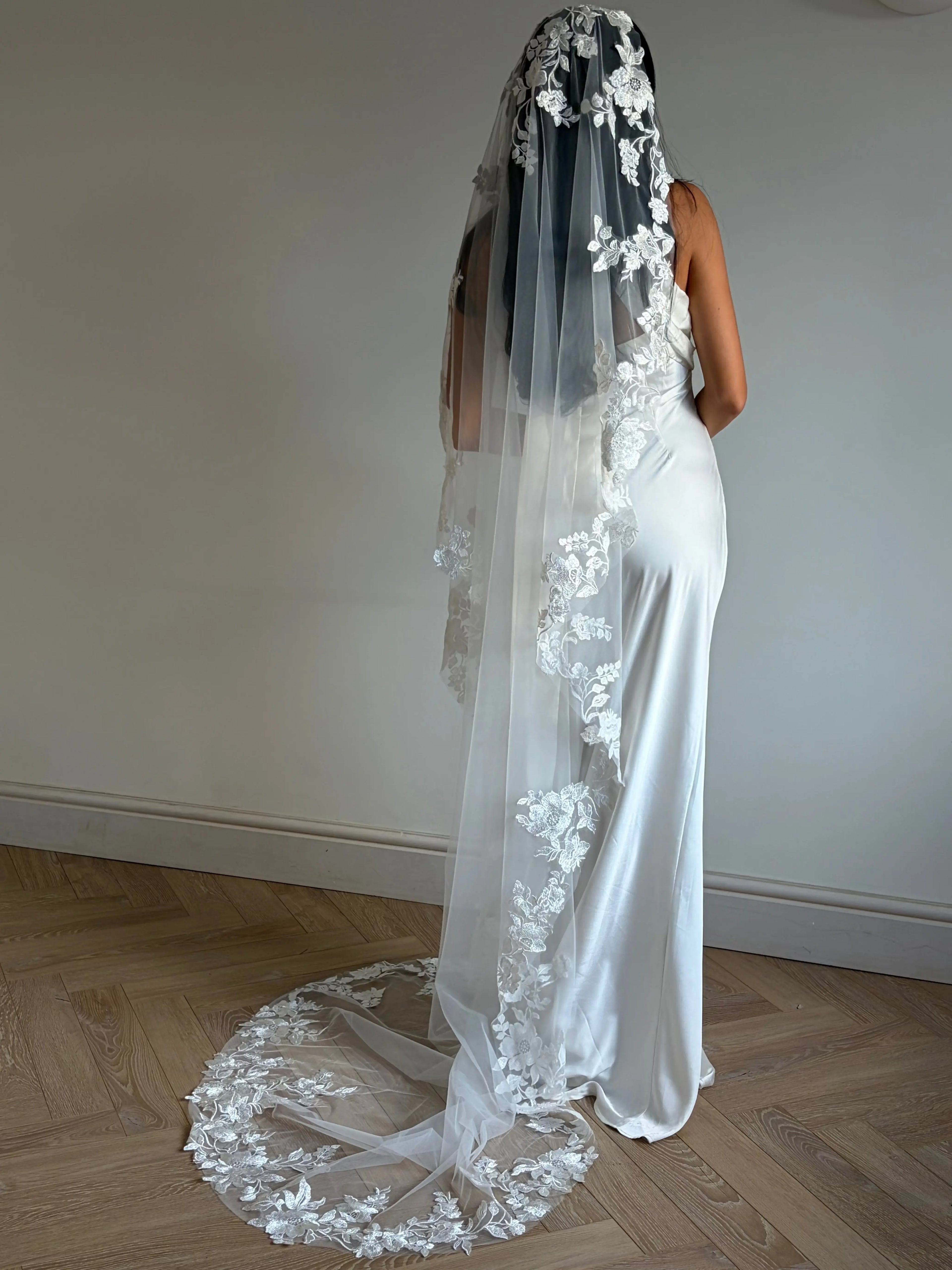 The Embroidered Ethereal Garden Floral Lace Veil features fine sequin embroidery and hand-finished floral lace trim for a soft, ethereal glow. Crafted from luxurious tulle in a soft off-white tone, this romantic bridal veil drapes beautifully for a fairytale-inspired finish. Perfect for garden or cathedral weddings.