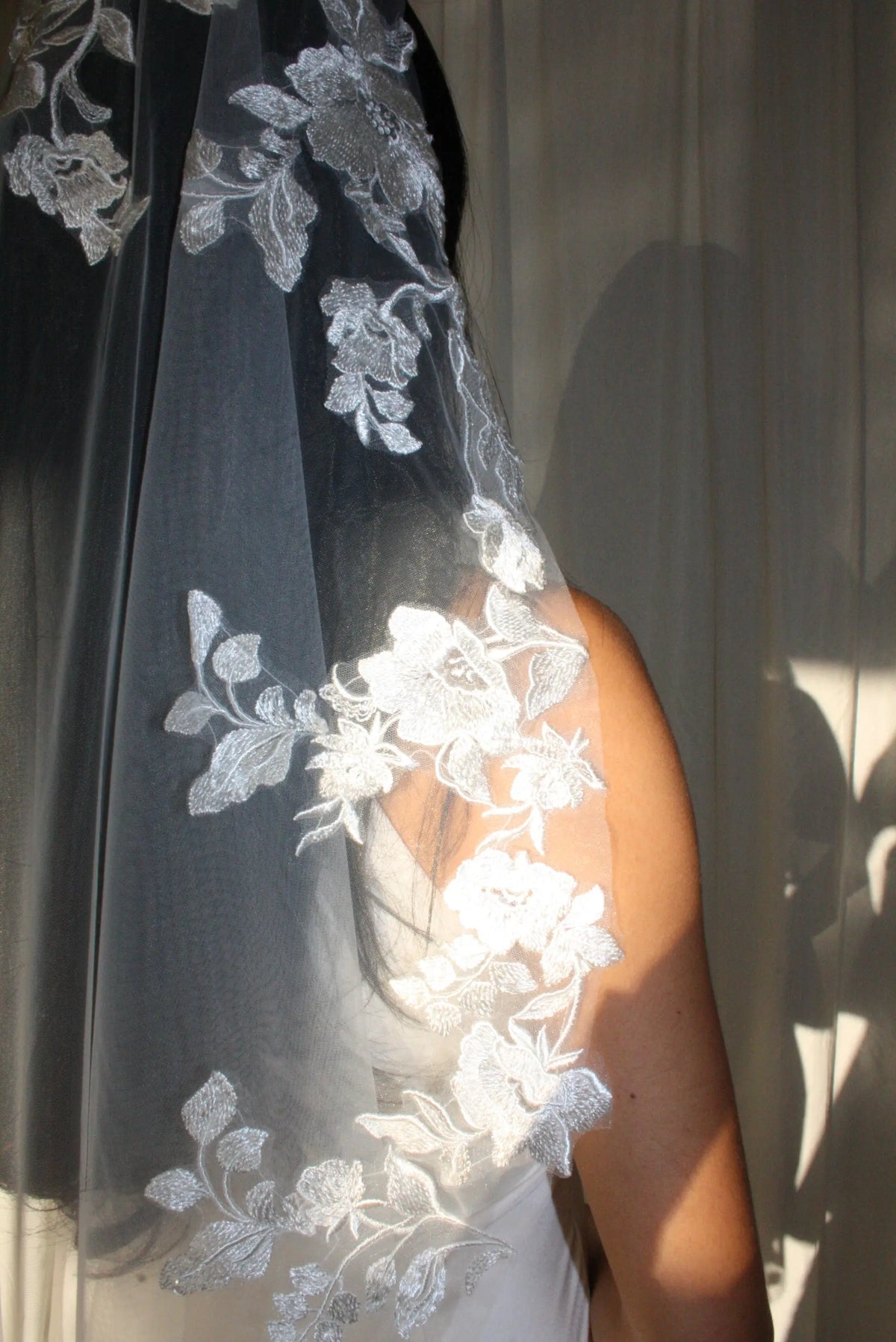 The Embroidered Ethereal Garden Floral Lace Veil features fine sequin embroidery and hand-finished floral lace trim for a soft, ethereal glow. Crafted from luxurious tulle in a soft off-white tone, this romantic bridal veil drapes beautifully for a fairytale-inspired finish. Perfect for garden or cathedral weddings.