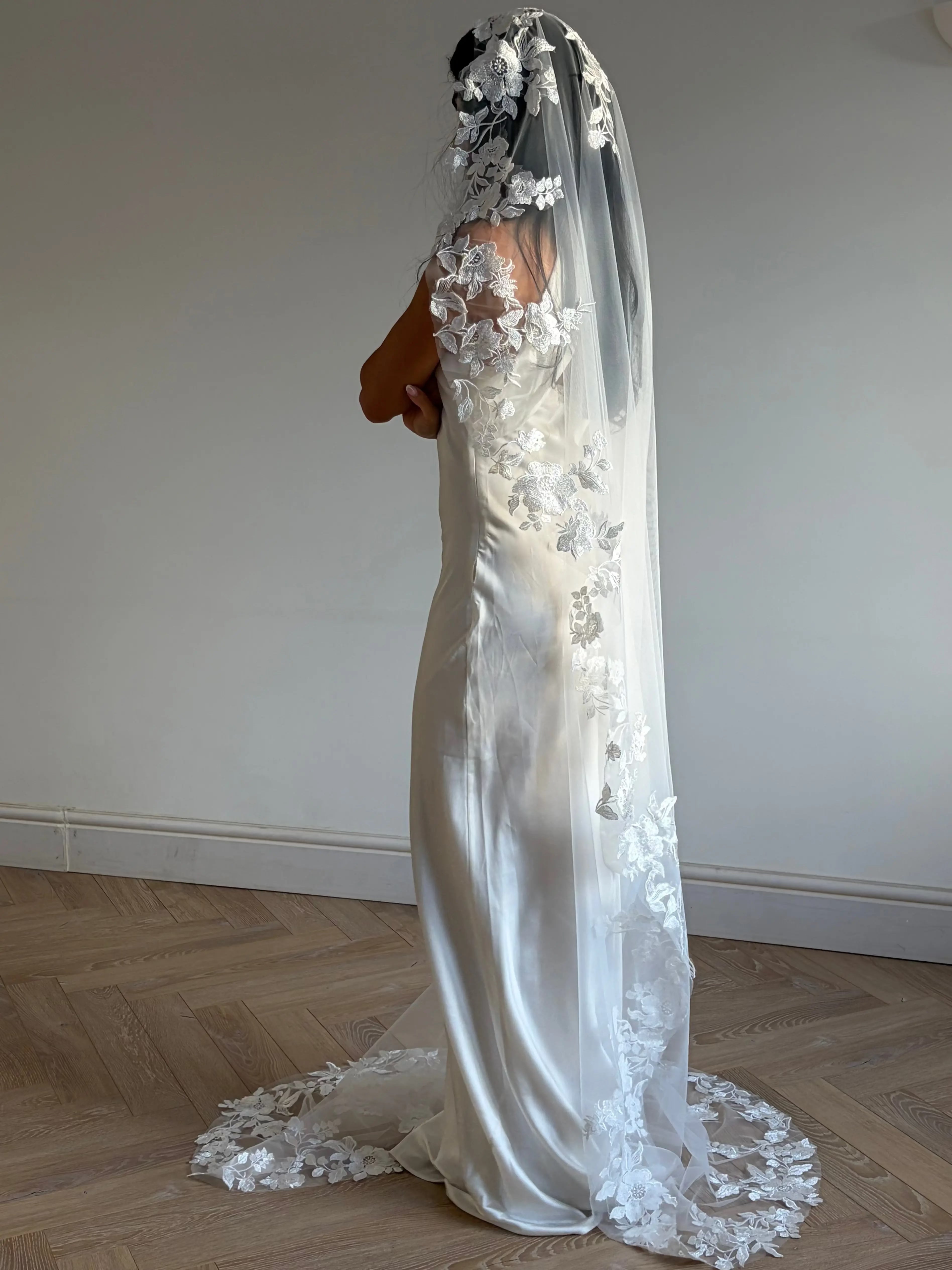The Embroidered Ethereal Garden Floral Lace Veil features fine sequin embroidery and hand-finished floral lace trim for a soft, ethereal glow. Crafted from luxurious tulle in a soft off-white tone, this romantic bridal veil drapes beautifully for a fairytale-inspired finish. Perfect for garden or cathedral weddings.