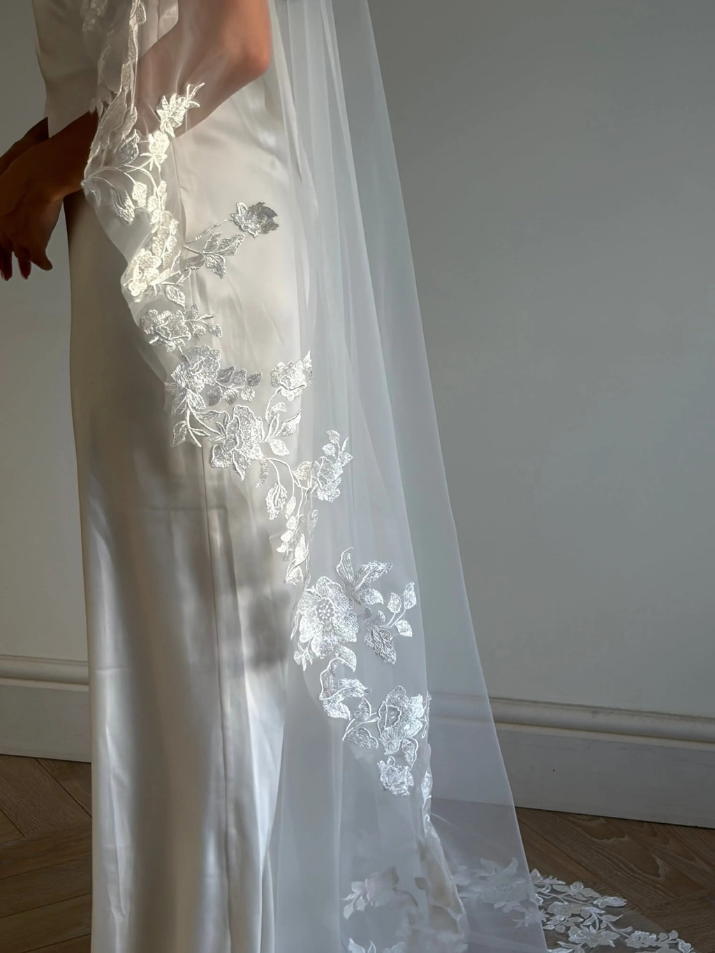The Embroidered Ethereal Garden Floral Lace Veil features fine sequin embroidery and hand-finished floral lace trim for a soft, ethereal glow. Crafted from luxurious tulle in a soft off-white tone, this romantic bridal veil drapes beautifully for a fairytale-inspired finish. Perfect for garden or cathedral weddings.