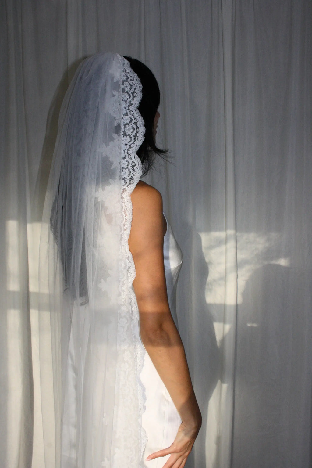 This pre-order lace trim bunched mantilla veil combines cathedral-length drama with hauntingly soft elegance. Made from luxurious, lightweight tulle and finished with fine lace edging, it falls straight to the ground in a flowing, cloak-like drape. Designed for brides seeking a romantic and timeless silhouette