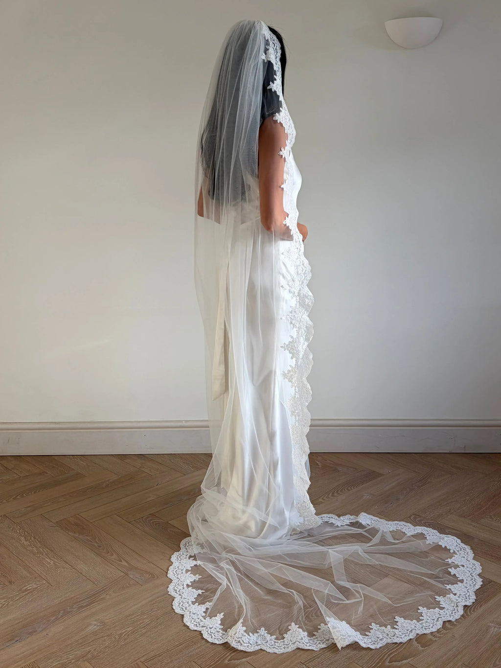 This pre-order lace trim bunched mantilla veil combines cathedral-length drama with hauntingly soft elegance. Made from luxurious, lightweight tulle and finished with fine lace edging, it falls straight to the ground in a flowing, cloak-like drape. Designed for brides seeking a romantic and timeless silhouette
