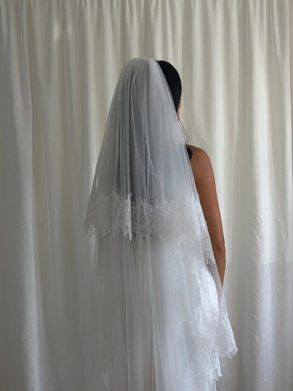 This vintage romantic blusher lace trim veil captures timeless bridal elegance. Made from luxuriously soft tulle, it features a delicate lace edge that frames the face and gown with effortless grace. The blusher layer adds a hint of vintage charm, creating a soft, ethereal silhouette ideal for traditional, chapel, or cathedral-length weddings. Perfect for brides seeking a romantic, classic look with refined detail and a seamless, airy drape.