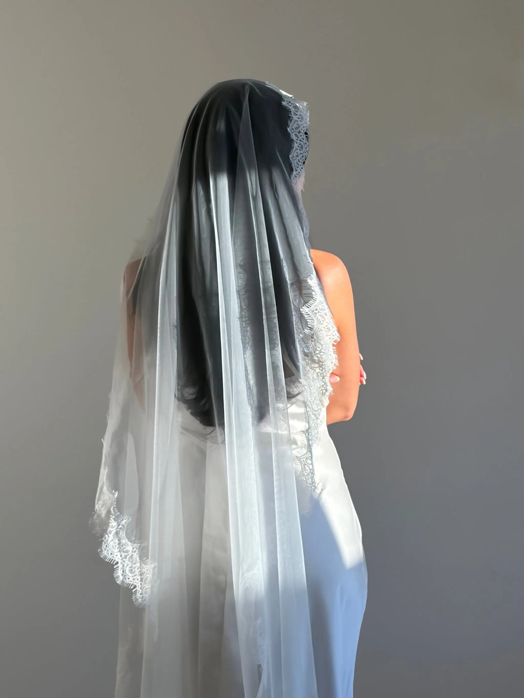 The Mantilla French Chantilly Lace Cathedral-Length Veil captures the romance of classic bridal style with exquisite craftsmanship and detail. Made from fine, lightweight tulle, this single-tier veil is bordered with intricate French Chantilly floral lace, complete with delicate eyelash edging that adds soft texture and movement. Its cathedral length creates a graceful, dramatic silhouette perfect for traditional or contemporary gowns. A hidden comb ensures a secure, comfortable hold, letting the veil flow 