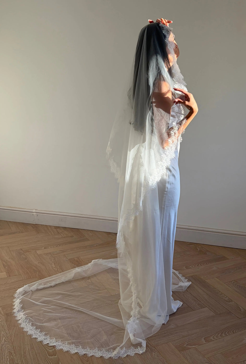 The Mantilla French Chantilly Lace Cathedral-Length Veil captures the romance of classic bridal style with exquisite craftsmanship and detail. Made from fine, lightweight tulle, this single-tier veil is bordered with intricate French Chantilly floral lace, complete with delicate eyelash edging that adds soft texture and movement. Its cathedral length creates a graceful, dramatic silhouette perfect for traditional or contemporary gowns. A hidden comb ensures a secure, comfortable hold, letting the veil flow 