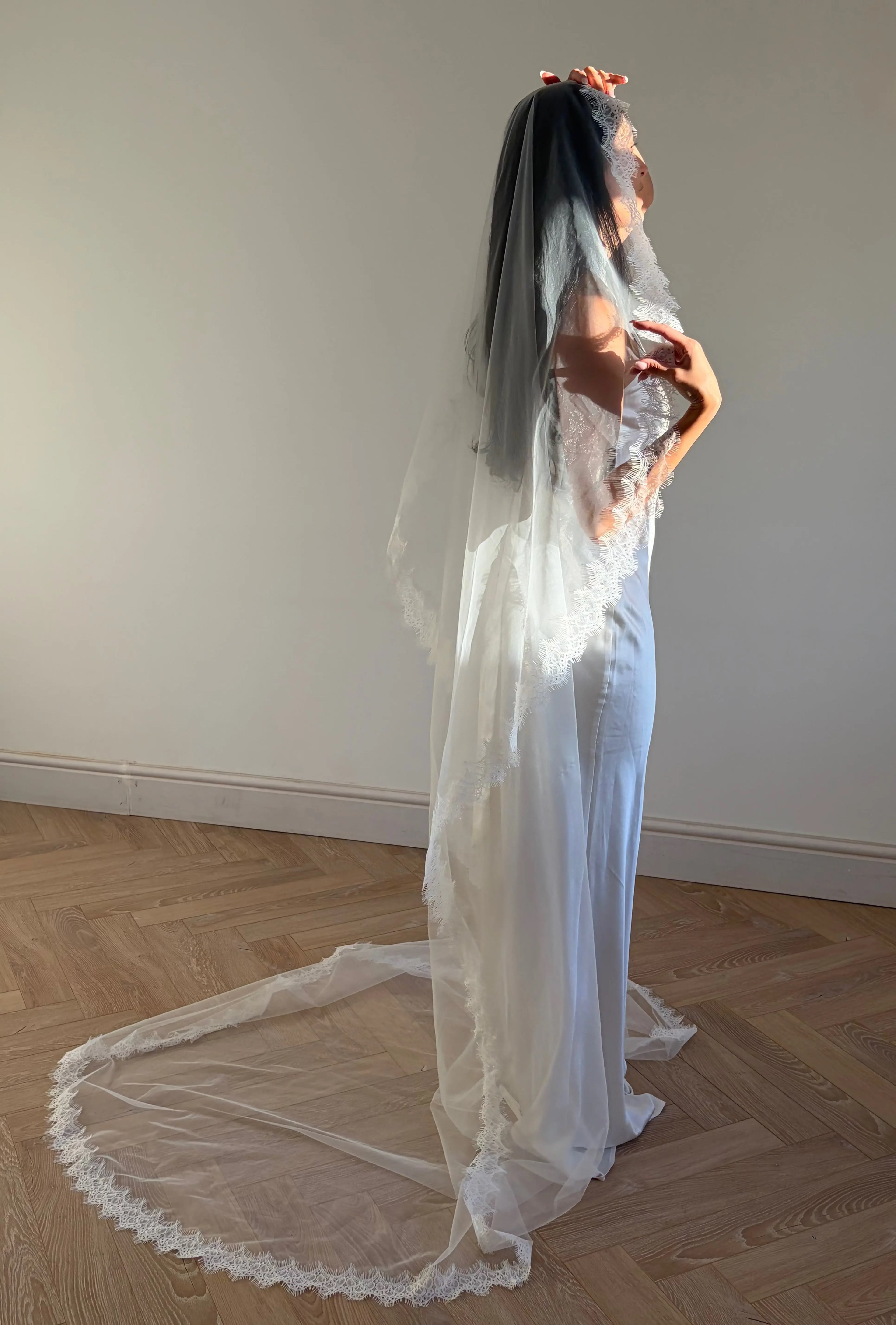 The Mantilla French Chantilly Lace Cathedral-Length Veil captures the romance of classic bridal style with exquisite craftsmanship and detail. Made from fine, lightweight tulle, this single-tier veil is bordered with intricate French Chantilly floral lace, complete with delicate eyelash edging that adds soft texture and movement. Its cathedral length creates a graceful, dramatic silhouette perfect for traditional or contemporary gowns. A hidden comb ensures a secure, comfortable hold, letting the veil flow 