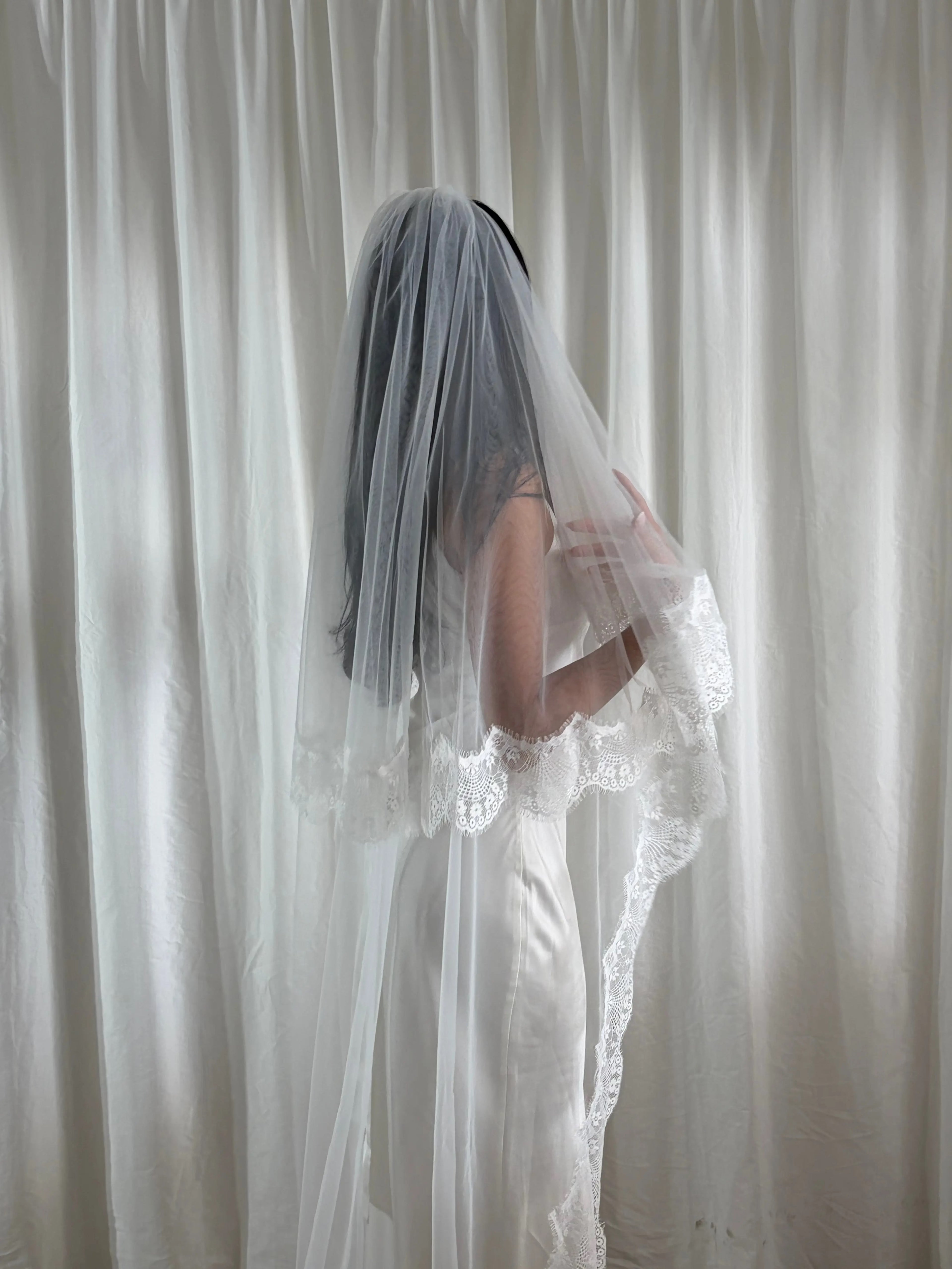 The Eyelash Trim Blusher Veil is a light, romantic accessory for modern brides seeking an ethereal finishing touch. Made from soft, flowing tulle, it features delicate eyelash lace along the edge for a subtle, feminine detail. The veil drapes softly over the face and shoulders, enhancing the bride’s silhouette with an airy, graceful effect. Its discreet comb attachment ensures a secure, seamless fit, making it ideal for both ceremony and photography. Perfect for adding a classic yet dreamy accent to any gow