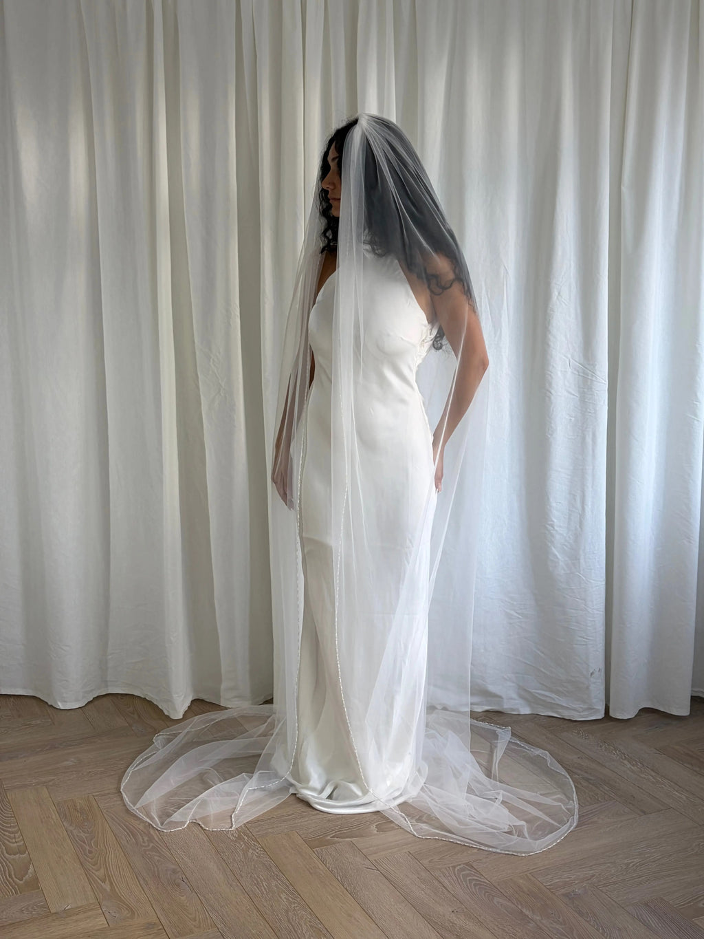 The Cathedral-Length Pearl Trim Veil features soft tulle and pearls & beads for a timeless, romantic bridal look. Lightweight and ethereal, it drapes beautifully for a graceful, luminous finish — perfect for modern or classic brides. The cloak-like full length veil finish is perfcet for the ethreal look.