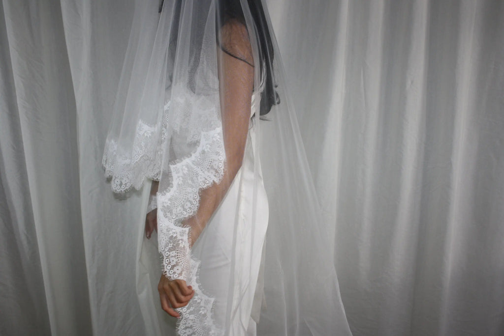 The Eyelash Trim Blusher Veil is a light, romantic accessory for modern brides seeking an ethereal finishing touch. Made from soft, flowing tulle, it features delicate eyelash lace along the edge for a subtle, feminine detail. The veil drapes softly over the face and shoulders, enhancing the bride’s silhouette with an airy, graceful effect. Its discreet comb attachment ensures a secure, seamless fit, making it ideal for both ceremony and photography. Perfect for adding a classic yet dreamy accent to any gow