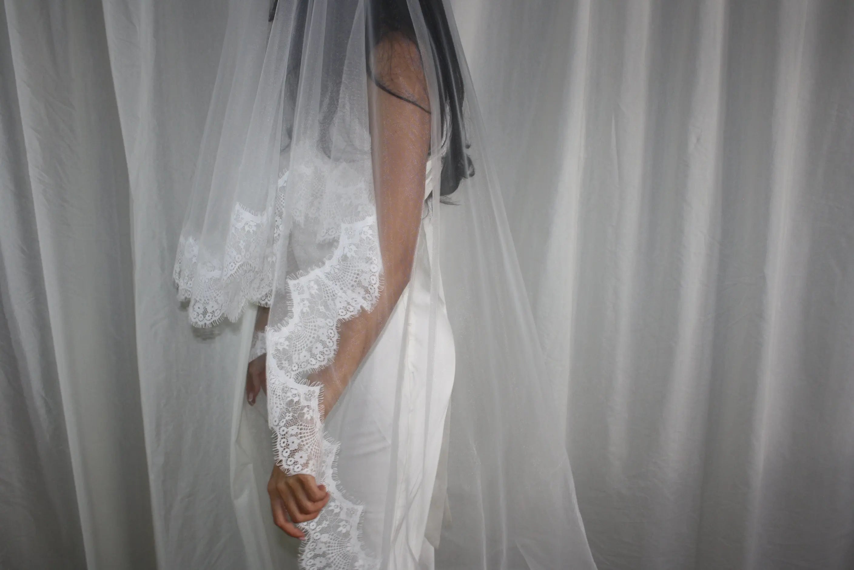 The Eyelash Trim Blusher Veil is a light, romantic accessory for modern brides seeking an ethereal finishing touch. Made from soft, flowing tulle, it features delicate eyelash lace along the edge for a subtle, feminine detail. The veil drapes softly over the face and shoulders, enhancing the bride’s silhouette with an airy, graceful effect. Its discreet comb attachment ensures a secure, seamless fit, making it ideal for both ceremony and photography. Perfect for adding a classic yet dreamy accent to any gow