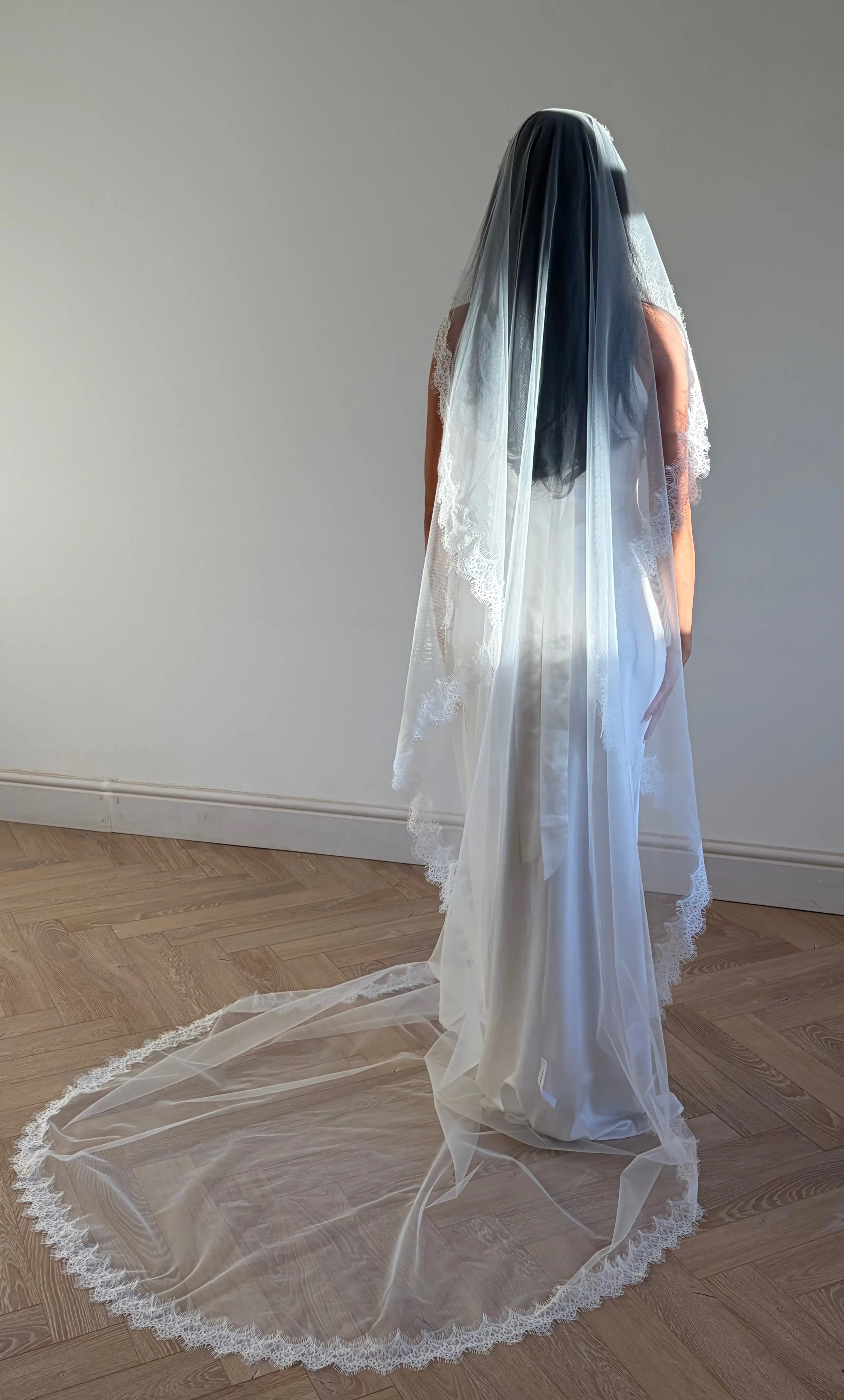 The Mantilla French Chantilly Lace Cathedral-Length Veil captures the romance of classic bridal style with exquisite craftsmanship and detail. Made from fine, lightweight tulle, this single-tier veil is bordered with intricate French Chantilly floral lace, complete with delicate eyelash edging that adds soft texture and movement. Its cathedral length creates a graceful, dramatic silhouette perfect for traditional or contemporary gowns. A hidden comb ensures a secure, comfortable hold, letting the veil flow 