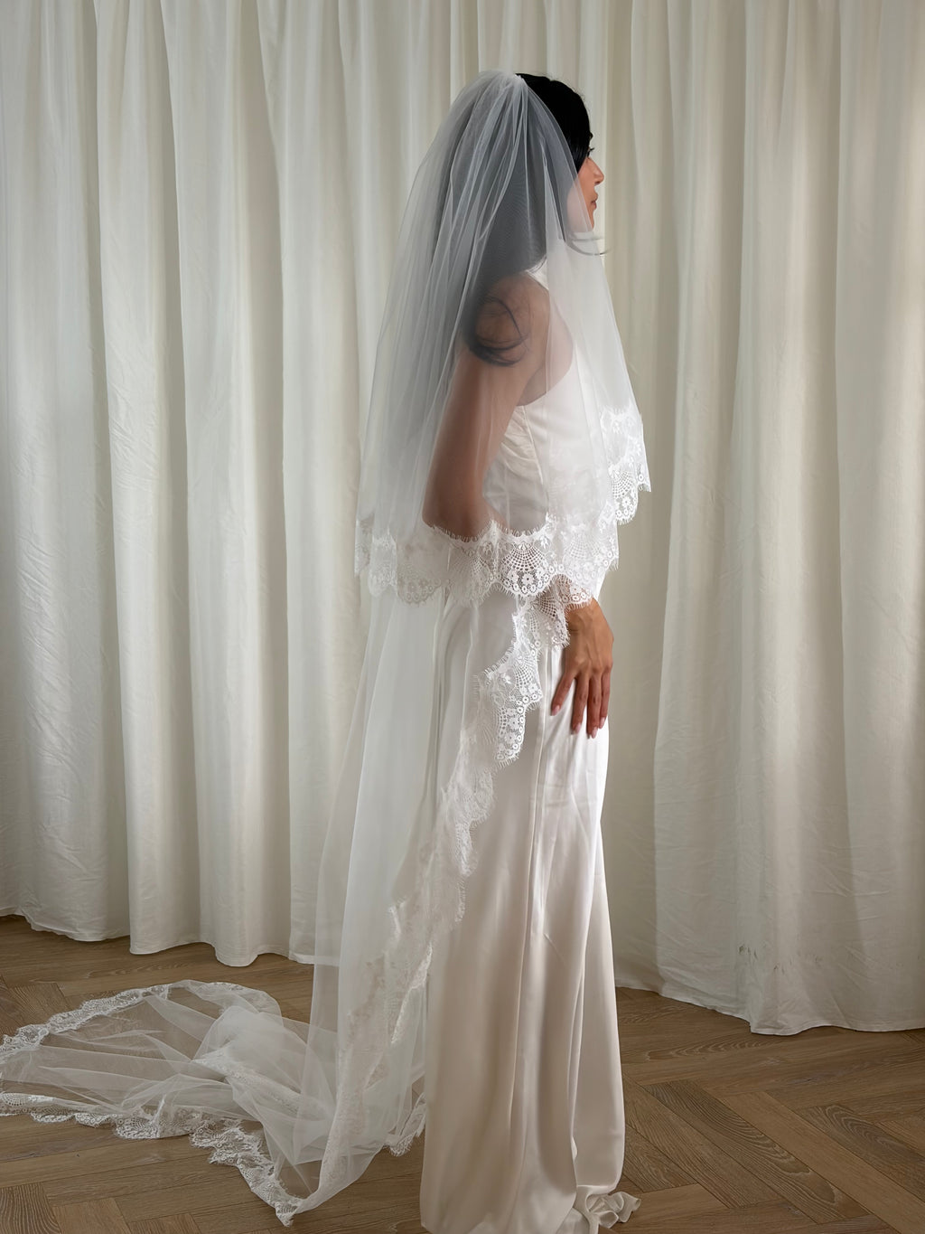 The Eyelash Trim Blusher Veil is a light, romantic accessory for modern brides seeking an ethereal finishing touch. Made from soft, flowing tulle, it features delicate eyelash lace along the edge for a subtle, feminine detail. The veil drapes softly over the face and shoulders, enhancing the bride’s silhouette with an airy, graceful effect. Its discreet comb attachment ensures a secure, seamless fit, making it ideal for both ceremony and photography. Perfect for adding a classic yet dreamy accent to any gow
