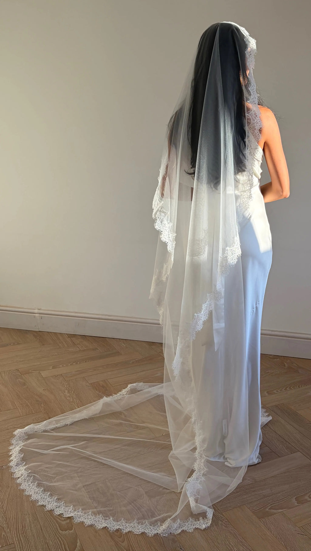 The Mantilla French Chantilly Lace Cathedral-Length Veil captures the romance of classic bridal style with exquisite craftsmanship and detail. Made from fine, lightweight tulle, this single-tier veil is bordered with intricate French Chantilly floral lace, complete with delicate eyelash edging that adds soft texture and movement. Its cathedral length creates a graceful, dramatic silhouette perfect for traditional or contemporary gowns. A hidden comb ensures a secure, comfortable hold, letting the veil flow 