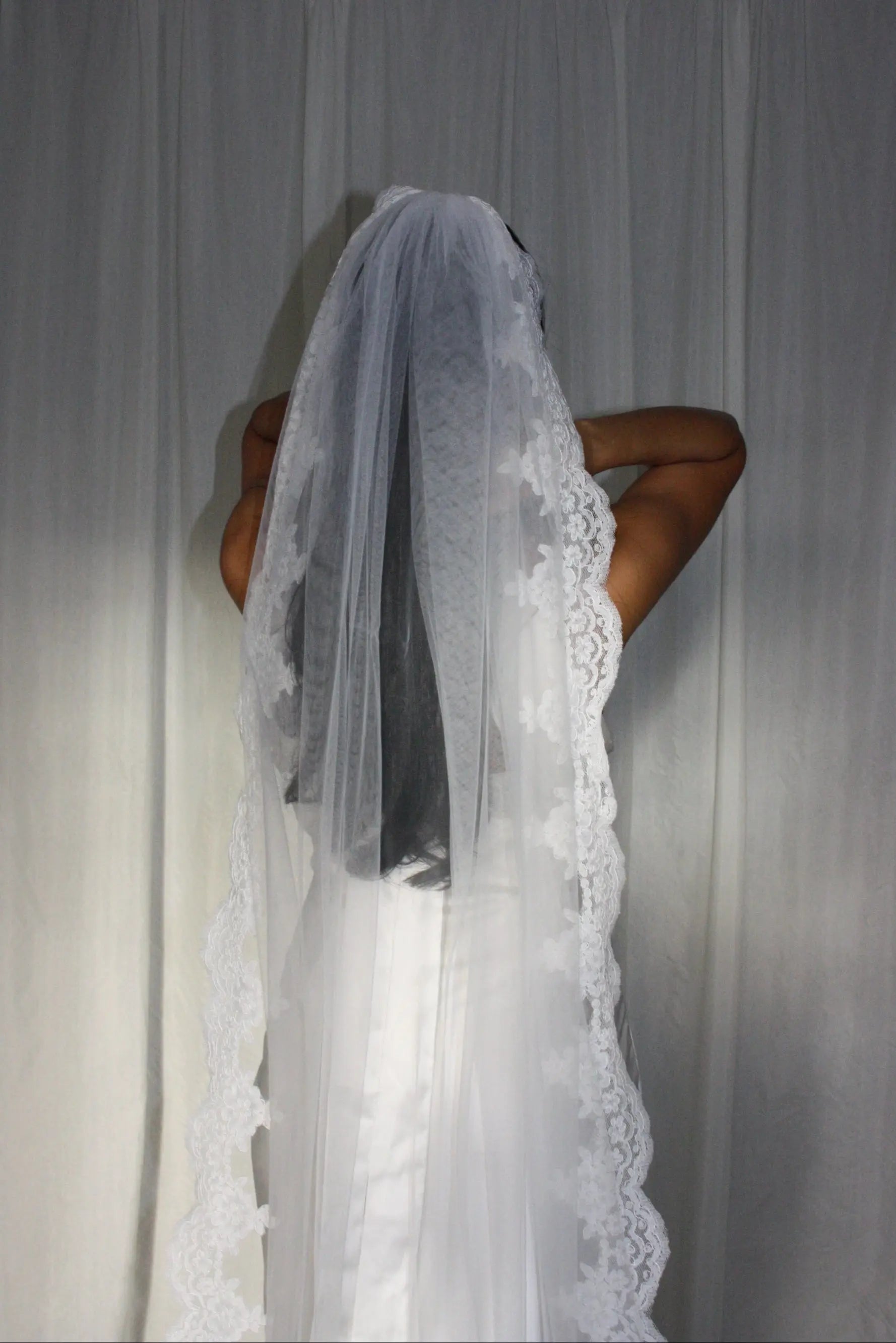 Lace trim bunched mantilla veil combines cathedral-length drama with hauntingly soft elegance. Made from luxurious, lightweight tulle and finished with fine lace edging, it falls straight to the ground in a flowing, cloak-like drape. Designed for brides seeking a romantic and timeless silhouette