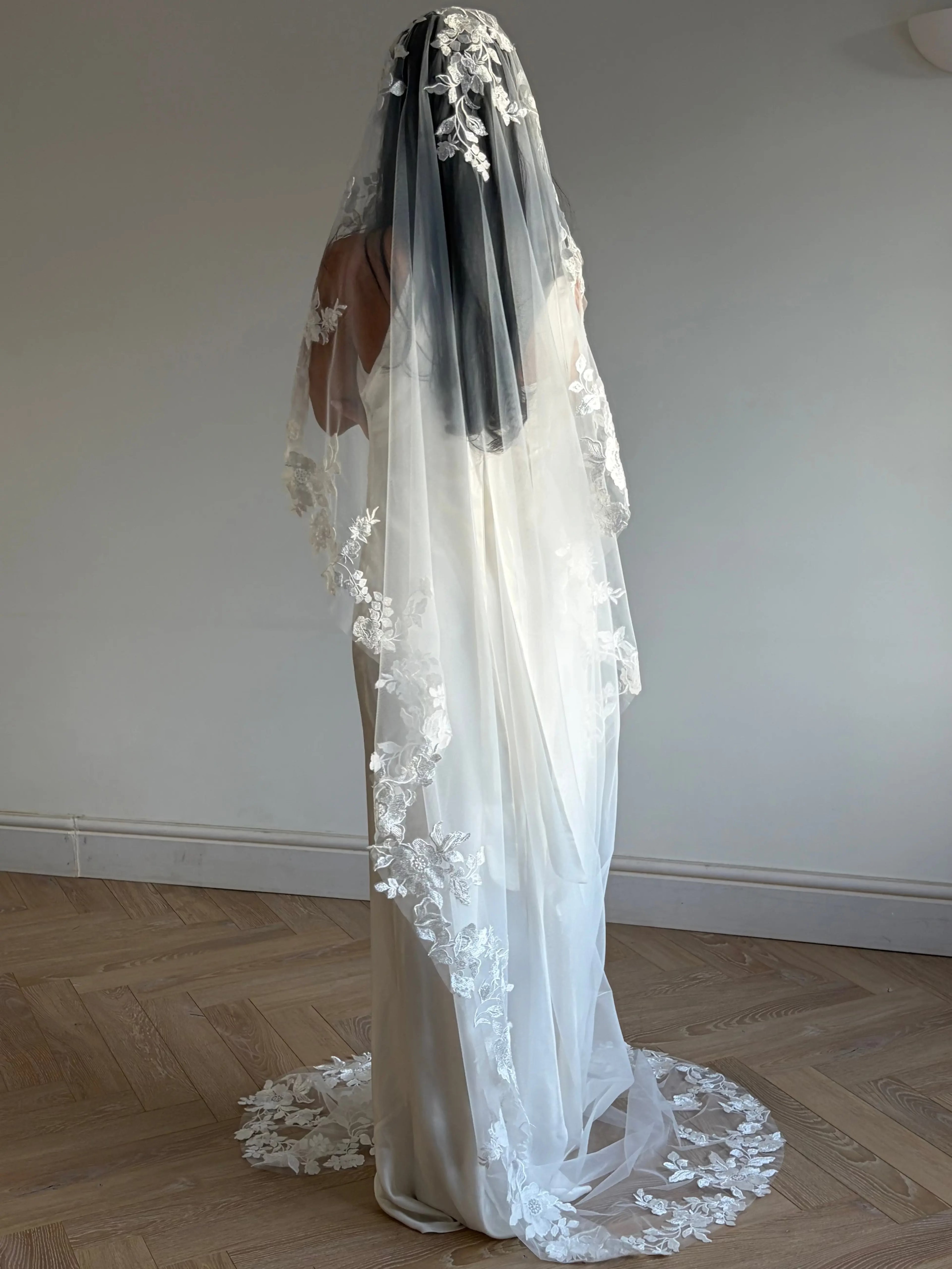 The Embroidered Ethereal Garden Floral Lace Veil features fine sequin embroidery and hand-finished floral lace trim for a soft, ethereal glow. Crafted from luxurious tulle in a soft off-white tone, this romantic bridal veil drapes beautifully for a fairytale-inspired finish. Perfect for garden or cathedral weddings.